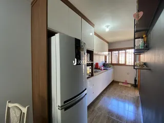 Vista interna de uma cozinha com armários brancos e eletrodomésticos em aço inoxidável.
