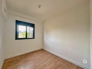 Ambiente interno de uma sala com piso de madeira clara e janela.