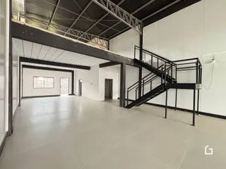 Imagem de um espaço interno amplo com estrutura de teto exposta e escadaria metálica.