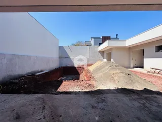 Vista externa de uma propriedade em construção com terra exposta e paredes brancas.