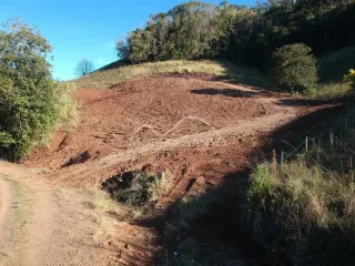 Vista de uma encosta de terra vermelha com vegetação rasteira.