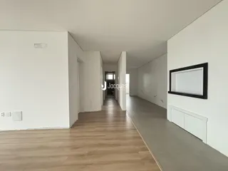 Corredor interno de uma residência com paredes brancas e piso de madeira clara.