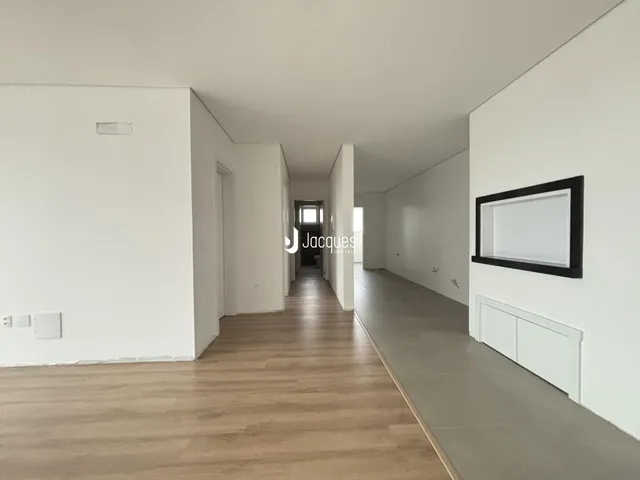 Corredor interno de uma residência com paredes brancas e piso de madeira clara.