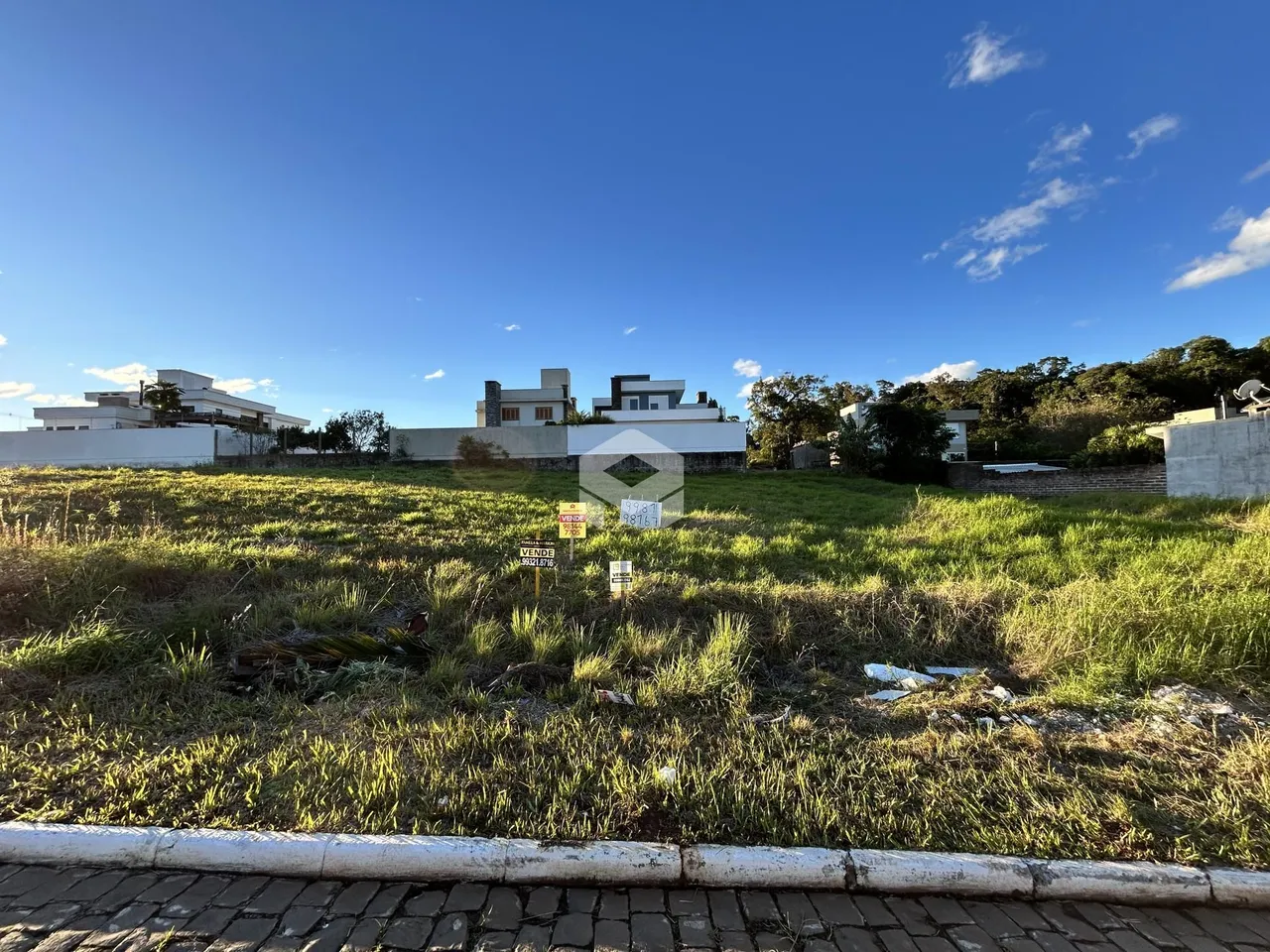 Vista externa de uma propriedade com terreno gramado e casas ao fundo.