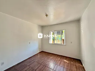 Vista interna de um cômodo com piso de madeira e paredes brancas.