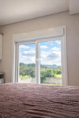 Uma vista externa de campos e vegetação é visível através de uma grande janela no quarto.