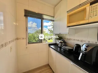 Cozinha com armários brancos e janela com vista para a vegetação externa.