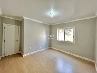 Ambiente interno de uma sala com piso de madeira clara e parede neutra.