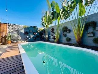 Piscina externa com deck de madeira e vegetação tropical.