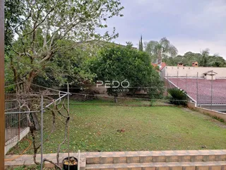 Vista externa de um terreno gramado com cerca e vegetação.