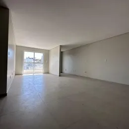 Sala de estar ampla com piso claro e paredes brancas, mostrando uma vista externa pela janela.