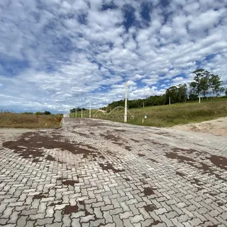 Vista da estrada pavimentada que leva a uma área rural com colinas ao fundo.