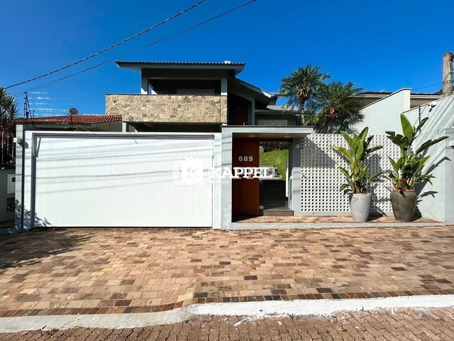 Fachada de uma casa em Lajeado, Brasil, com garagem branca e piso de tijolos.