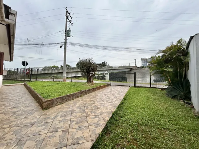 Vista externa de um terreno com jardim e calçada de piso cerâmico.
