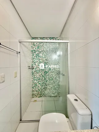 Banheiro com box de vidro e revestimento mosaico verde.
