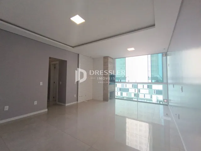 Ambiente interno de uma sala ampla com piso claro e grandes janelas.