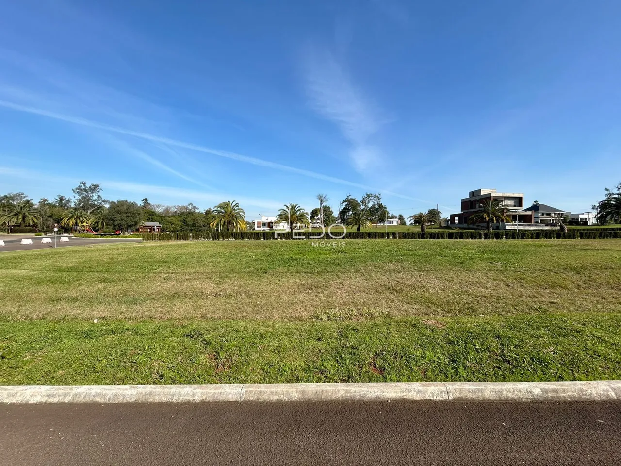Vista de um campo gramado com residências ao fundo sob um céu azul.