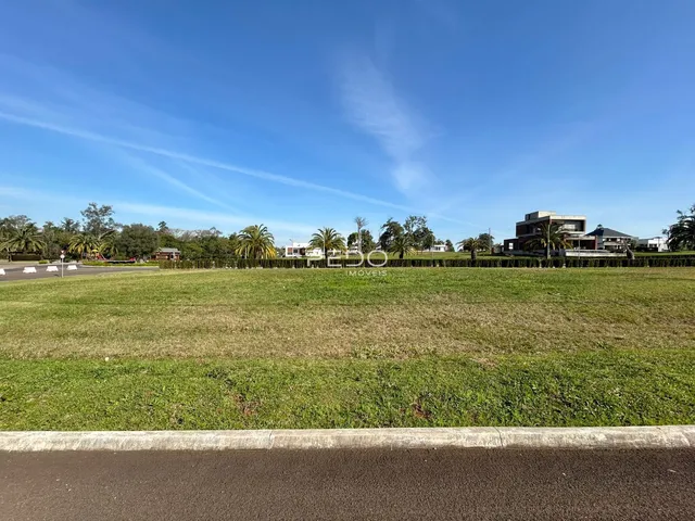 Vista de um campo gramado com residências ao fundo sob um céu azul.