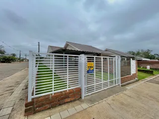 Foto da fachada de uma residência com portão branco e muro de tijolos.