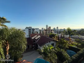Vista externa de uma residência com telhado de telhas vermelhas e vegetação tropical.