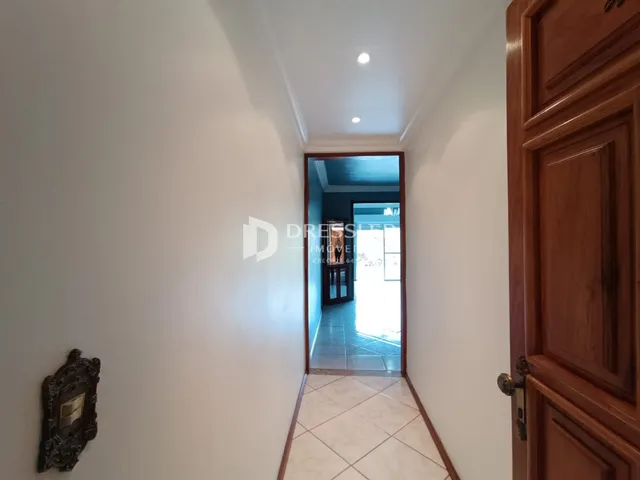 Corredor interno de uma residência com paredes brancas e piso de cerâmica clara.
