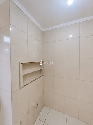 Parede revestida com azulejos claros e uma prateleira embutida.