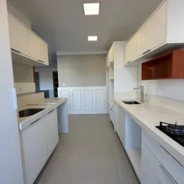 Cozinha com armários brancos e bancadas claras.