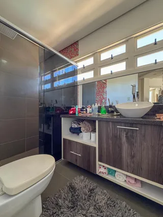 Foto do interior de um banheiro com box de vidro e bancada de madeira.