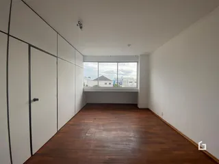 Corredor interno com piso de madeira e janela de vista para o exterior.
