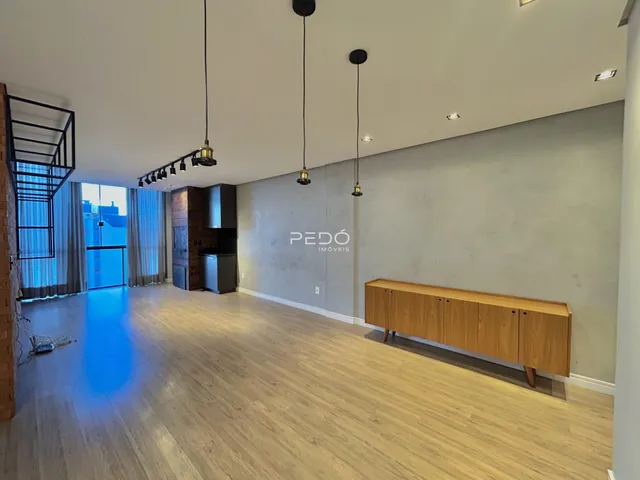 Sala de estar ampla com piso de madeira clara e teto alto.