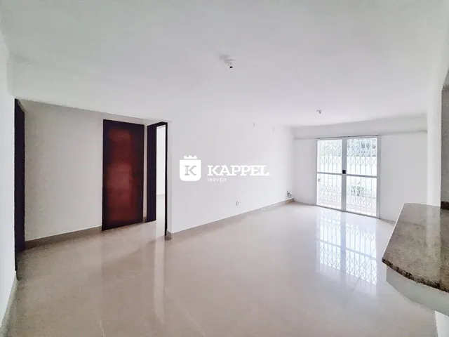 Ambiente interno de uma sala ampla com piso claro e iluminação natural.