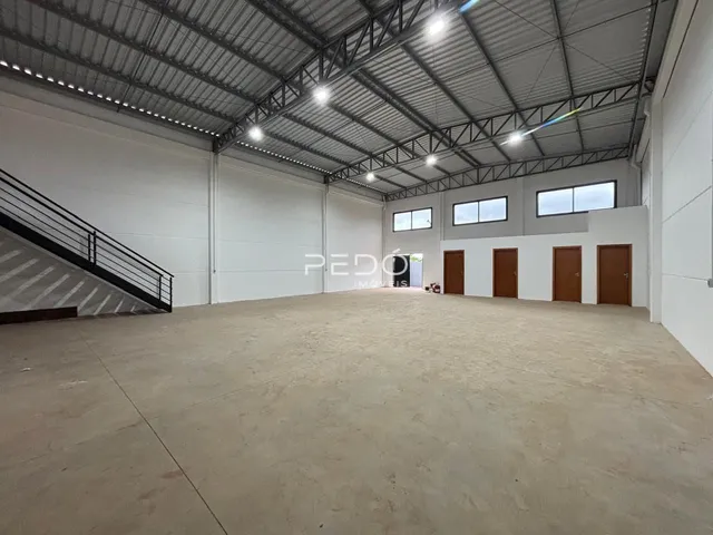 Vista interna de um grande espaço industrial com teto metálico e piso de concreto.