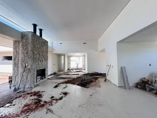 Interior de uma área em construção com paredes brancas e piso exposto.