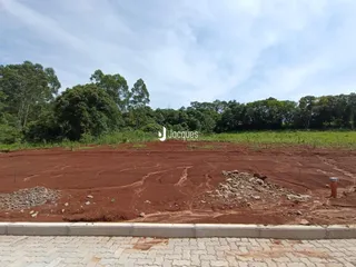 Imóvel de terreno com solo de terra vermelha e vegetação ao fundo.