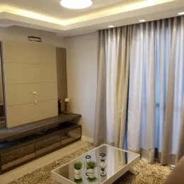 Sala de estar com cortinas claras e móveis escuros.