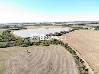 Vista panorâmica de campos abertos e um corpo d'água em uma propriedade rural.