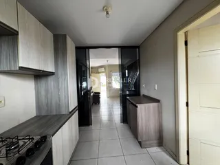 Vista interna de uma cozinha com armários e piso de cerâmica em um apartamento.
