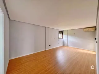 Ambiente interno de uma longa sala com piso de madeira clara e paredes brancas.