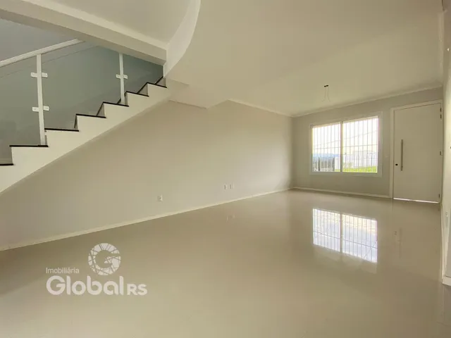 Ambiente interno de uma sala ampla com escada e grande janela.