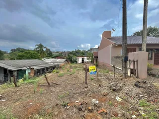 Vista externa de uma propriedade com terreno baldio e edificações ao fundo.