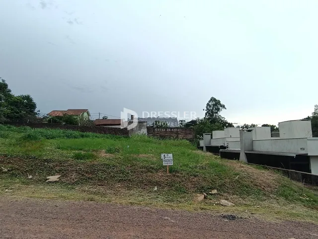 Vista externa de uma propriedade com terreno gramado e construções ao fundo.