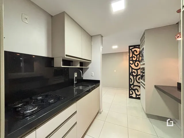 Cozinha com armários brancos e bancada escura é visível na imagem.