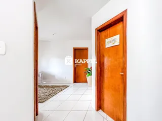 Hall de entrada com piso de cerâmica branca e portas de madeira.
