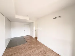 Vista interna de um corredor com paredes brancas e piso de madeira clara.