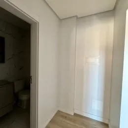 Foto de um corredor interno com paredes brancas e piso de madeira clara.