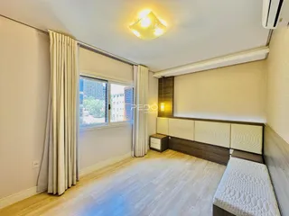 Quarto com piso de madeira clara e janela com cortinas na Lajeado.