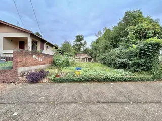 Vista externa de uma residência com muro de tijolos e vegetação no quintal.