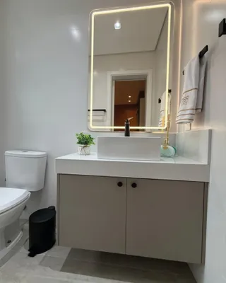Banheiro moderno com bancada branca e espelho iluminado.