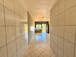 Corredor interno com piso de cerâmica claro que leva a uma área externa.