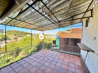 Uma varanda com piso de ladrilhos vermelhos e vista para a paisagem verde.